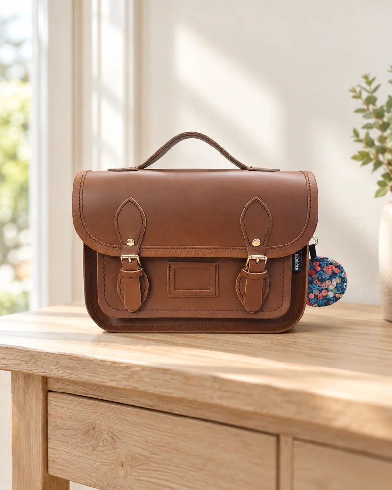 Chestnut Zatchels mini satchel with twin buckles and a floral charm on an entryway console