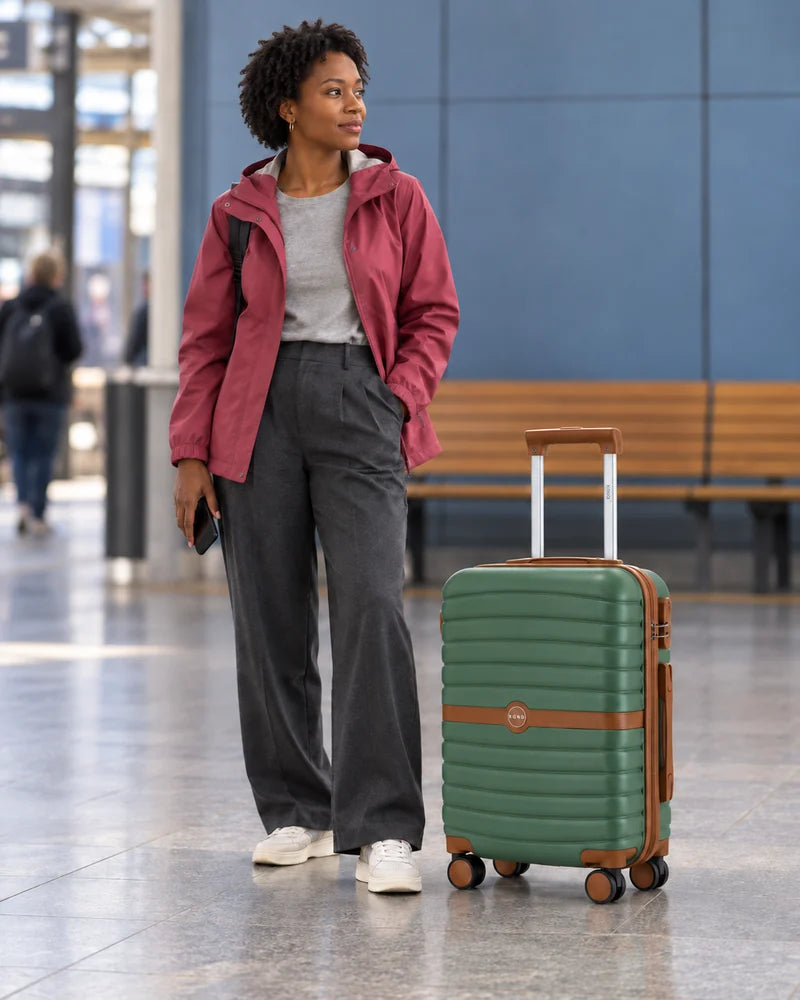 Woman waiting at a station beside a green cabin suitcase with brown trim